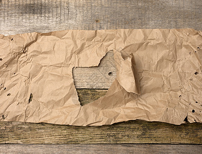 一张撕破的棕色纸 木板上的木质背景上有一个洞图片