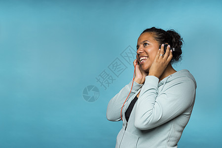年轻 有吸引力的混合种族青年妇女 享受听用耳机倾听音乐的蓝色背景彩色音乐家混血耳朵唱歌女性化卷发工作室成人摇滚图片