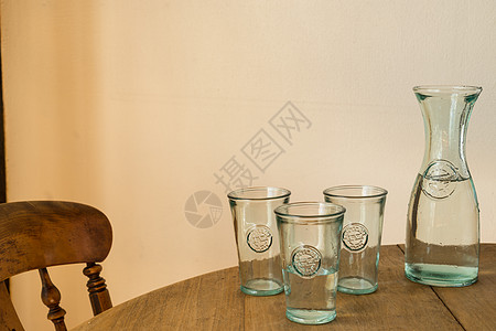 玻璃瓶或加水罐 在木制桌子和室内椅子上装三个杯子图片