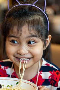 吃面条的亚洲女童 孩子吃拉面微笑着享受食物 孩子吃意大利面女孩勺子家庭美食午餐营养头巾筷子杯子图片