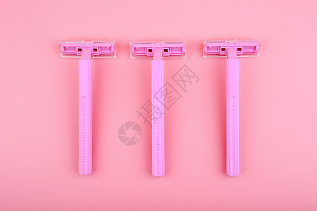 在粉红背景下刮剃须的三件塑料剃刀的最顶部视图图片