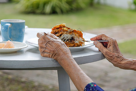 年长妇女在后院吃早餐手臂退休祖母疗养院皮肤老年奶奶成人食物房子背景图片