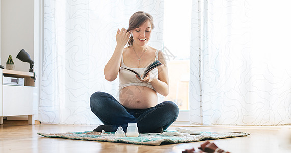 关于怀孕的阅读 快乐的怀孕妈妈坐在地板上 看书母亲投标牛仔裤拥抱孩子们孩子婴儿学习父母肚子图片