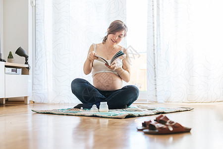 关于怀孕的阅读 快乐的怀孕妈妈坐在地板上 看书孩子们母性孩子母亲牛仔裤幸福拥抱地面父母肚子图片
