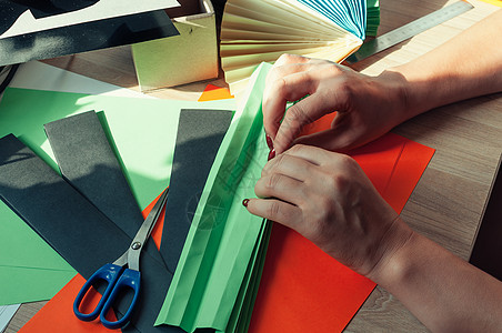 在前景中 女性的手正在为折纸扇 彩色纸片和木桌上的剪刀准备空白 一个风扇的几个空白 用于设计 广告或文本的模板班级播放叶子艺术爱图片