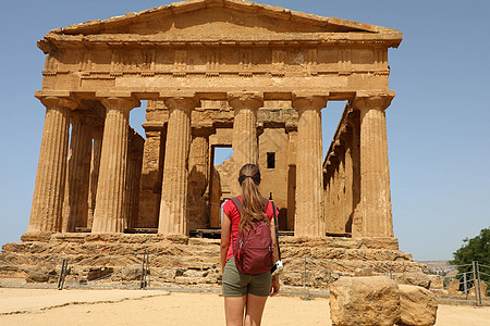 年轻妇女在西西里Agrigento寺谷的Concordia寺庙观望 旅行者女孩参观意大利南部的希腊寺庙相机访问大理石废墟反光镜女图片