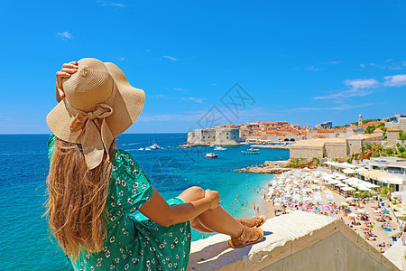 欧洲克罗地亚Dubrovnik 令人惊叹的全景色村落 她身着帽子坐在墙上防御女性建筑学女士全景工事村庄假期旅游城市图片