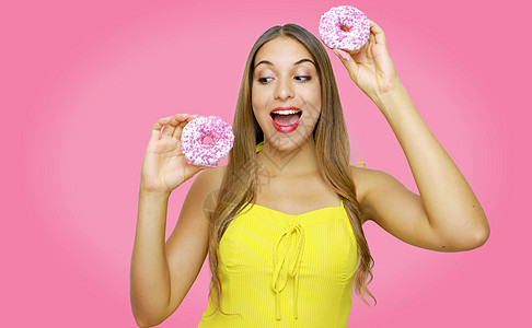 漂亮有趣的女孩 看上去很快乐 而且拿着粉红背景的甜甜圈图片