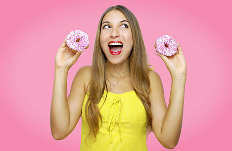 紧贴可爱的女孩拿着甜甜圈 仰望着粉红色背景的一面图片