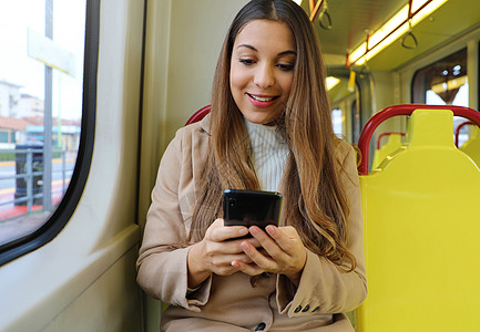年轻女性的短信 智能手机坐在电车上城市外套电话火车技术阅读消息微笑拉丁民众图片