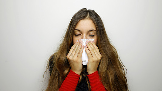 女孩在灰色背景上吹鼻涕 站立于灰色背景之下咳嗽症状感染喷嚏鼻子冷冻手帕卫生女性流感图片