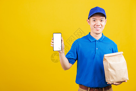 身穿蓝制服的送货服务人员微笑着笑脸 手持纸集装箱 装有外卖袋包食品包和显示智能手机屏幕命令工人职业商业邮递员专营蔬菜杂货店男人图片