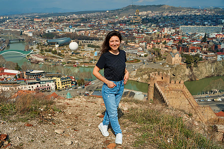 一个可爱的黑发女孩从山丘上 享受着第比利斯的美丽景色 全城都在她脚下蓝色街道市中心堡垒天线建筑中心地标景观天际图片