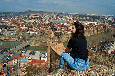 一个可爱的黑发女孩从山丘上 享受着第比利斯的美丽景色 全城都在她脚下历史性建筑天空堡垒旅行大教堂天线地标教会旅游图片