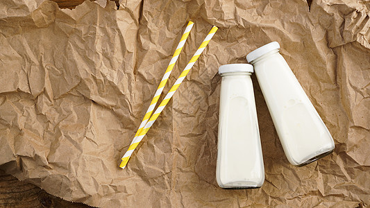 玻璃瓶中的有机奶牛 两瓶牛奶在压碎的手工艺纸上瓶子奶油乳糖木头饮料市场玻璃产品早餐小吃图片