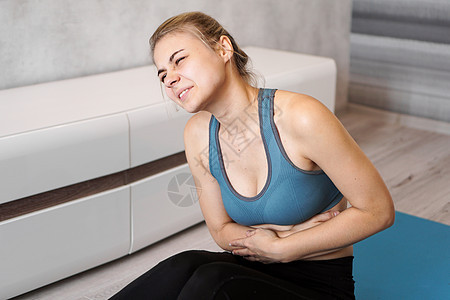 年轻妇女坐在瑜伽垫上 在训练后触摸肚子的肖像图片