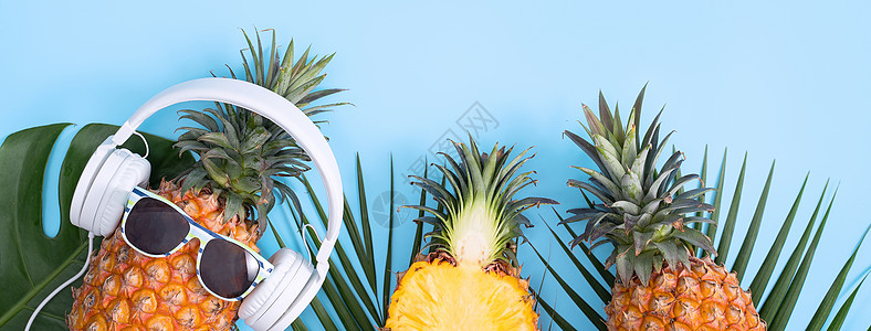 穿着白色耳机的有趣的菠萝 听音乐的概念 与热带棕榈叶隔绝在彩色背景上 高视线 平板设计潮人海滩太阳镜叶子蓝色水果高架音乐乐趣平铺图片
