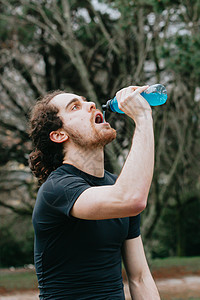 一个年轻的运动运动员在公园里喝碳酸盐饮料 同时健身图片
