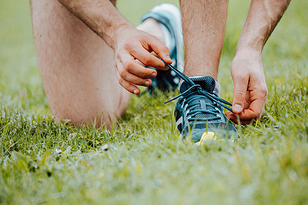 一个超近身的男子 绑紧鞋带在运动鞋上 在训练健身前用绿草对着绿草踪迹赛跑者活力女性身体娱乐小路培训师太阳阳光图片