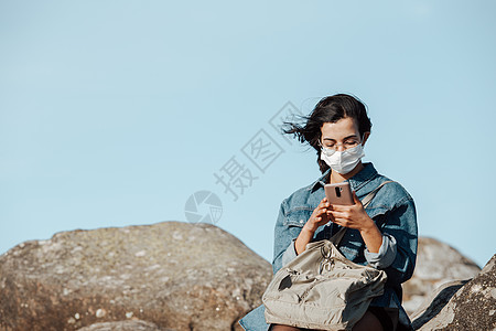 一名戴面罩检查其手机的年轻女子 而风与复制空间同时吹响图片