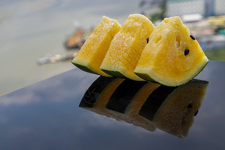 鲜多汁的黄西瓜在黑色亚克力板上切成三角形 具有反射和自然景观图片