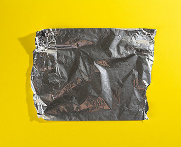 一张皱巴巴的灰色箔纸 用于包装黄色背景上边缘撕裂的产品图片