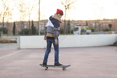 在沥青游乐场玩花样的滑板男孩 青少年滑板男孩微笑娱乐运动诡计溜冰者城市羊毛帽木板行动休闲装图片