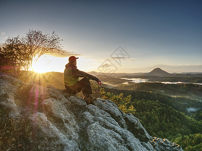 登山者在顶峰休息 旅行者穿绿色防风外套r力量运动男子薄雾身材悬崖远足者游客岩石男人图片