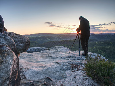 摄影师在岩石上的三脚架上拍照远足山峰照片职业圆顶薄雾地平线帝国悬崖背包图片
