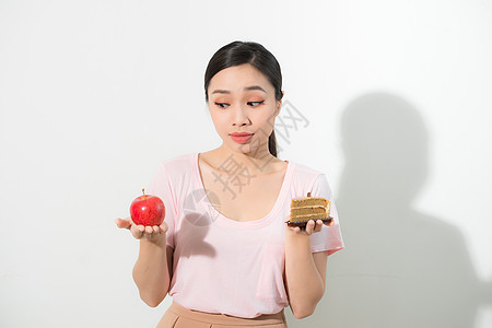 女人手里拿着蛋糕甜食和苹果水果选择 试图抵制诱惑 做出正确的饮食选择 减肥饮食困境暴食概念白色女性重量女孩营养食物甜点图片