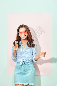 高兴的是 带着露齿微笑的可爱亚洲年轻女性看着镜头 拿着美味的冰淇淋 站在浅粉色背景中 身着旅游装 戴着眼镜女士头发胡扯甜点白色美图片