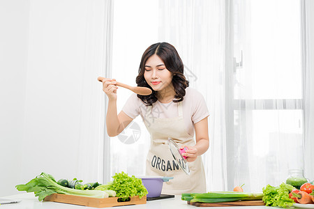 美丽的年轻女子在家里用蔬菜煮汤的肖像 笑声女性厨师女士家庭主妇勺子围裙白色女孩厨房黄色图片