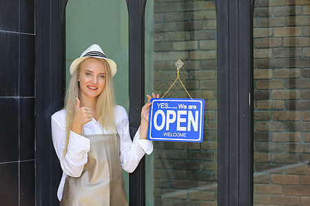 充满自信的年轻女性商店的肖像 小商业咖啡店老板站在店门前并挂有开放牌子女孩窗户餐厅木板食堂食物快乐女士咖啡顾客图片