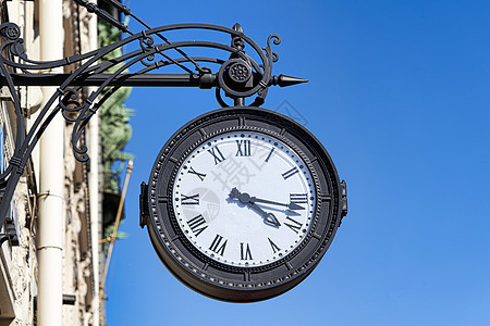 有罗马数字的古色古香的圆的时钟在cit的街道上垂悬蓝色手表白色拨号圆圈时间金属商业小时民众图片
