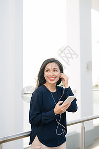 这是我最喜欢的歌 迷人的年轻黑发女孩在夏日露台咖啡厅坐着时 在电话里听音乐 很吸引人音乐播放器女性城市旅行成人潮人街道技术音乐女图片