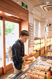 当地面包店的帅哥拿着一个托盘 上面放着面包或馅饼 购买甜点消费主义顾客盘子食物咖啡店零售羊角店铺成人时间男性男人图片