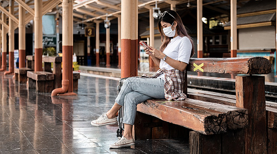亚洲旅游少女带着面具等待远程火车站使用智能手机 社交媒体报到 单身旅行者 暑假铁路探险概念 校对 Portnoy图片