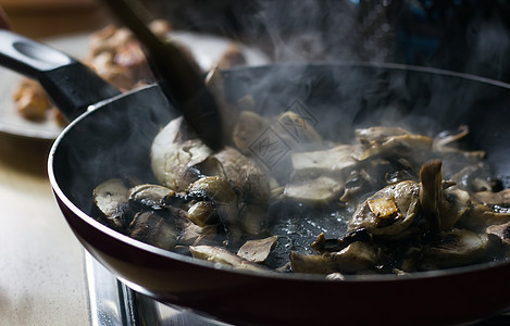 新鲜切开蘑菇的顶端景色正在煎锅中煮熟 蒸汽出来 木勺子用于混合蔬菜 展示家用烹饪素的概念图片