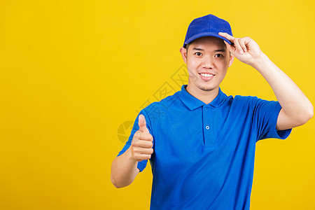 身穿蓝色T恤衫和帽子制服微笑 手举大拇拇指的手势工作室导游衬衫衣服职业运输商业船运工作工人图片