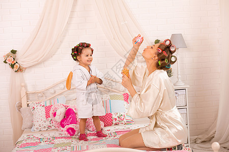 一个迷人的小女孩和她妈妈戴着卷发器玩肥皂球 妇女节 这个女孩和她妈妈玩得很开心母亲微笑孩子女性幸福乐趣喜悦浴衣快乐女士图片
