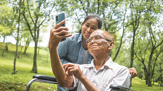 坐在轮椅上的祖父和孙女通过公园智能手机与亲戚交谈的视频电话 度假家庭生活 请访问InfoFinland上的生活家庭假期减值花园享图片