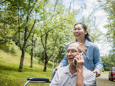 快乐的残疾老人用智能手机聊天 而孙女在公园里推着轮椅 假期的家庭生活男人回忆家庭退休祖父机动性男性技术花园照顾者图片