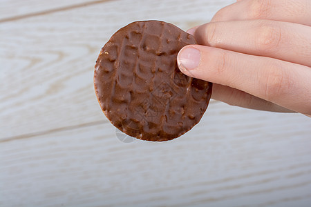 手握着一个巧克力 覆盖的饼干 在木制背景棕色白色蛋糕小吃糖果木头圆形食物涂层甜点图片