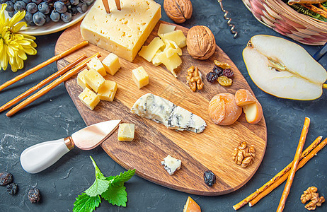 不同种类奶酪的奶酪盘 — 埃门塔尔奶酪 自制奶酪 帕尔马干酪 蓝纹奶酪 面包条 核桃 葡萄干 梨 桌上的葡萄图片