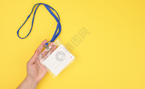 女性手拿着黄色背景上蓝色挂绳上的透明塑料徽章图片