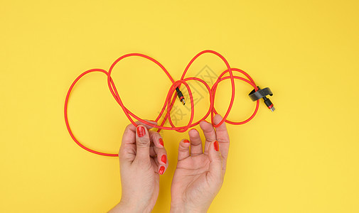 女性手持扭曲电缆 在黄色背景的红色纺织包装纸上为移动装置充电;妇女手持图片