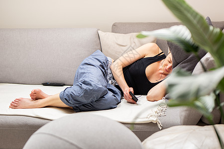 疲倦的年轻女子休息 躺在舒适的沙发上 用手机在客厅里放大垫子图片