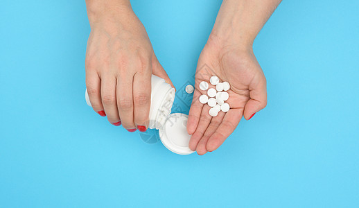 女性手拿着圆圆白药片 在蓝色背景下 止痛治疗图片