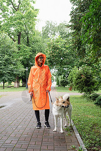 穿着橙色雨衣的年轻女子与她的狗在公园里散步友谊闲暇下雨乐趣伴侣宠物幸福猎犬动物成人图片