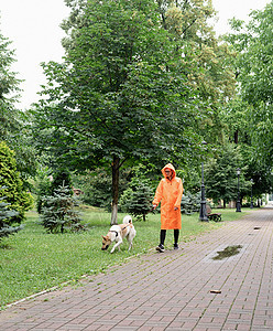 穿着橙色雨衣的年轻女子与她的狗在公园里散步宠物友谊犬类街道朋友闲暇幸福伴侣天气动物图片